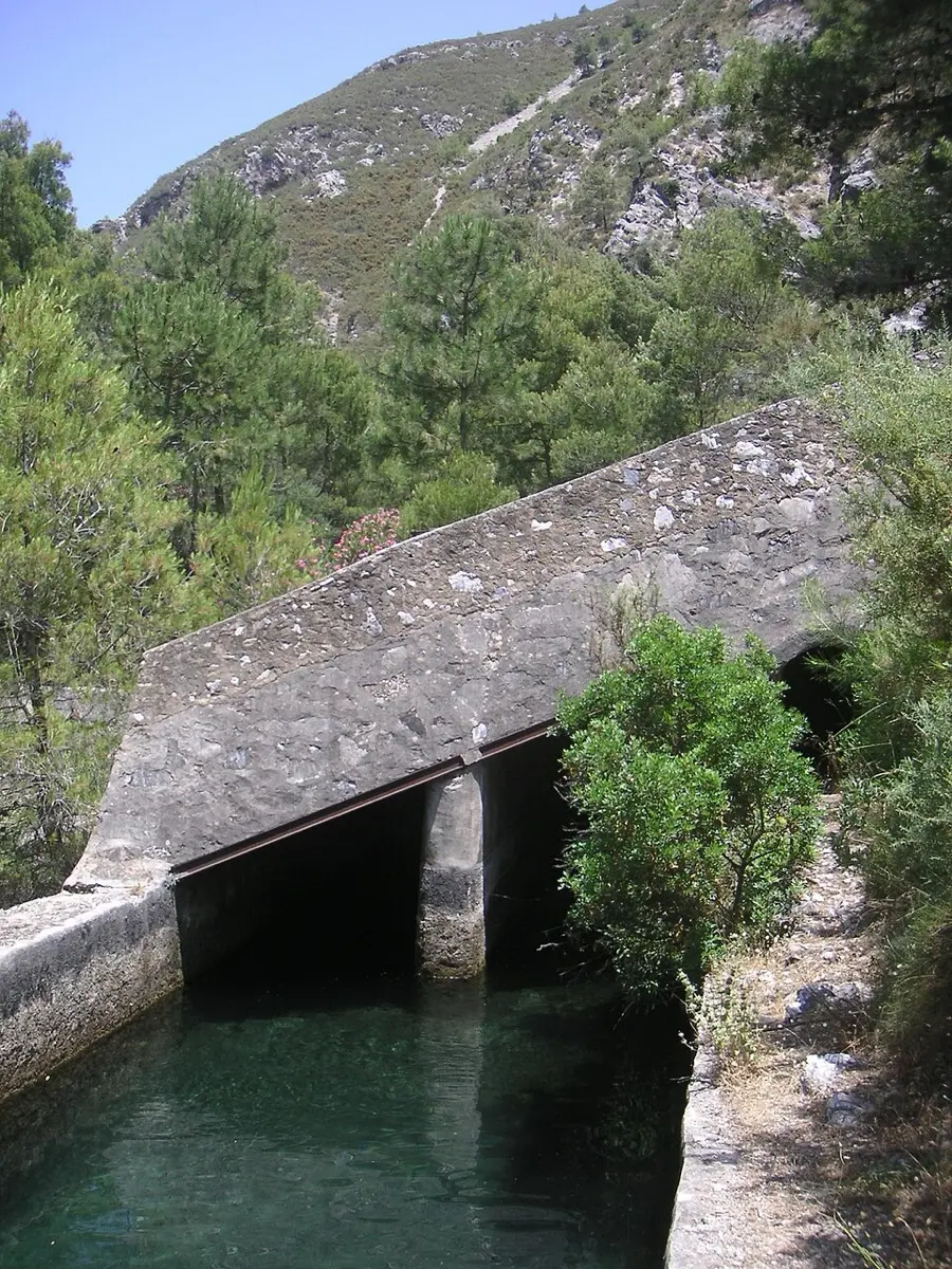 Pequeña presa de piedra con un canal de agua verde en el valle del Chíllar