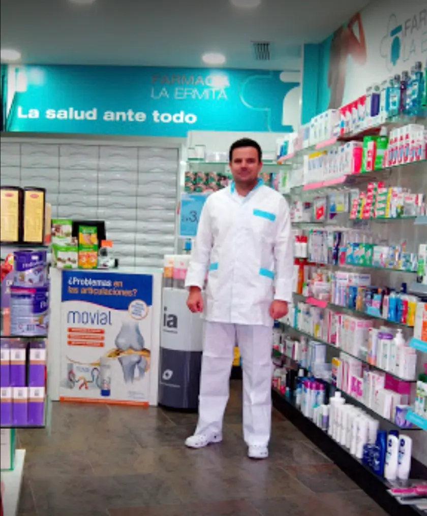 Farmacéutico con bata blanca en el pasillo de la farmacia, entre expositores de productos