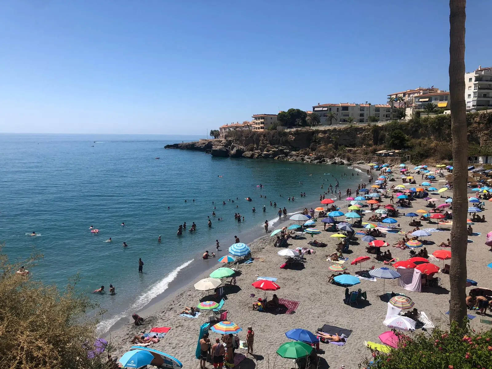 La playa El Salón llena de sombrillas en verano, bajo los acantilados con casas