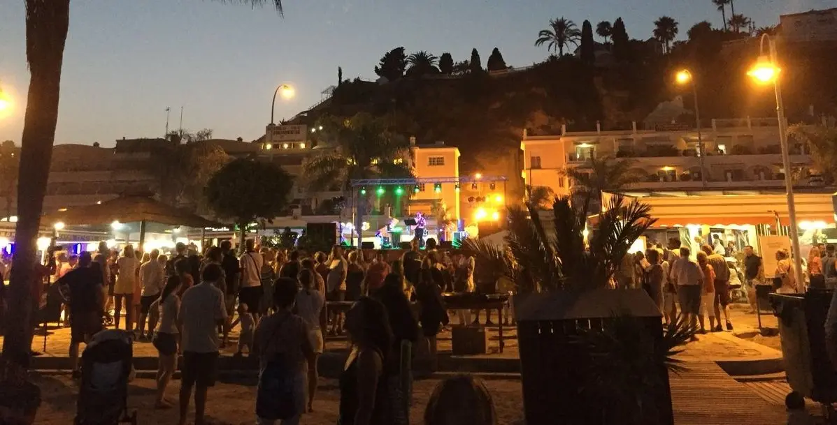 Público ante un escenario con luces en el paseo de la playa al anochecer en la Noche de San Juan