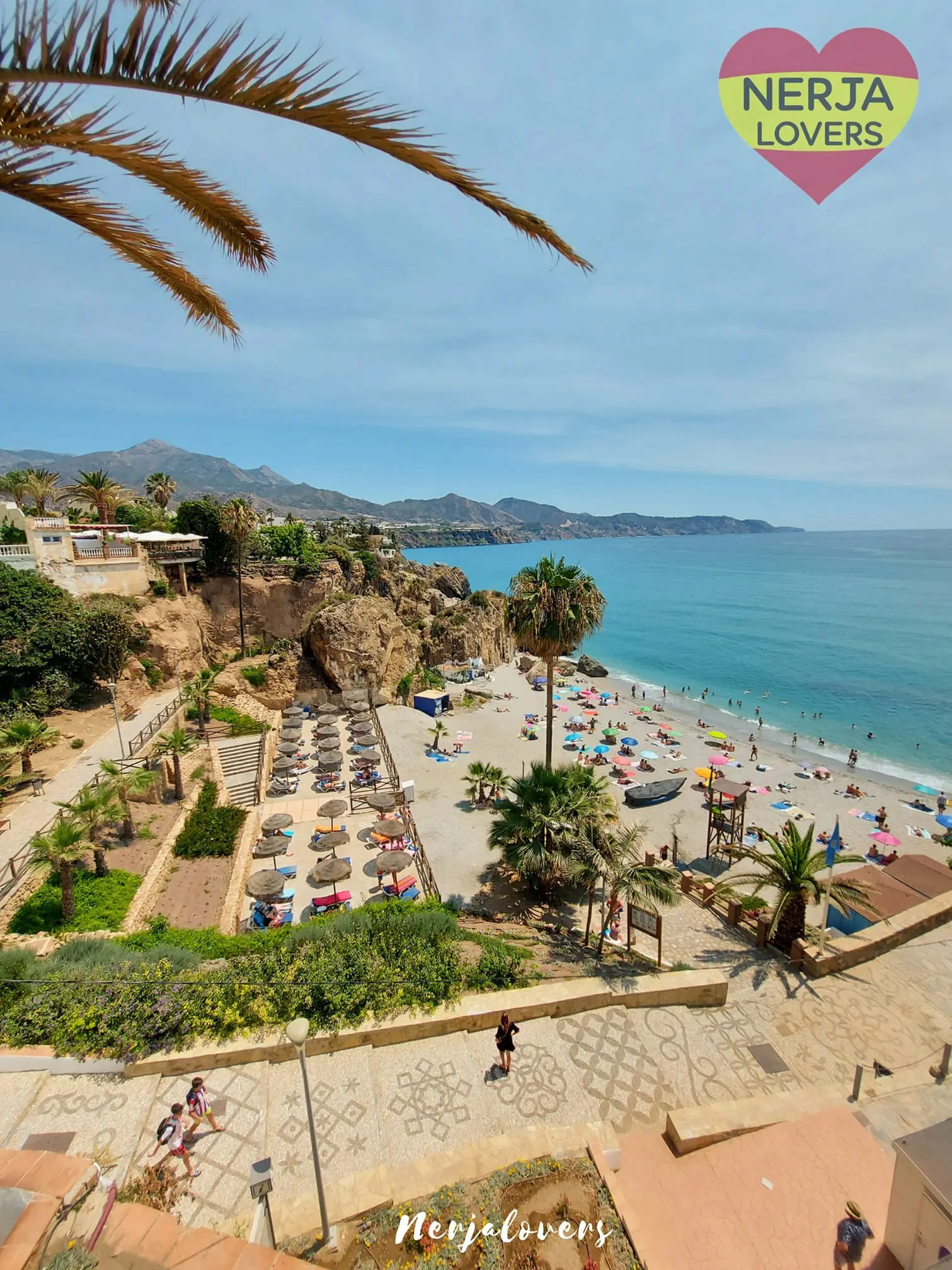 Bajada empedrada con mosaico hacia la playa de Calahonda, con hamacas y barcas en la arena