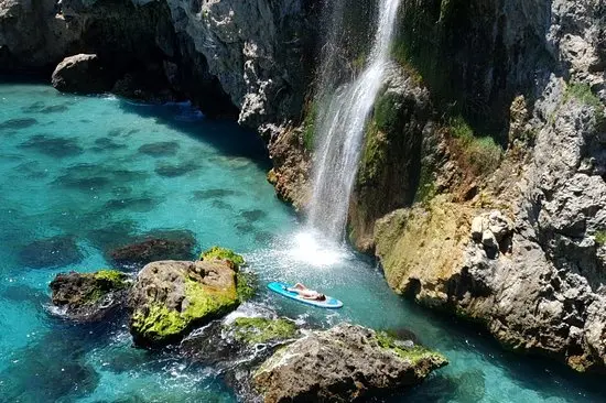 Persona tumbada en una tabla de pádel surf junto al chorro de la cascada