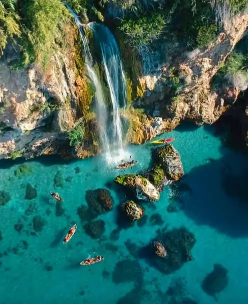 Vista cenital de la cascada con kayaks rojos y amarillos entre rocas cubiertas de verdín