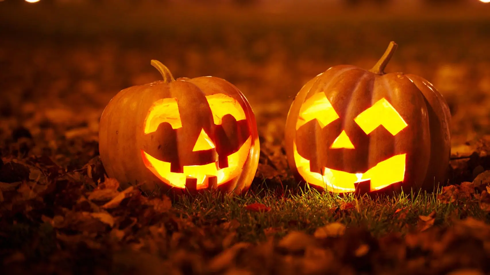 Dos calabazas de Halloween talladas e iluminadas sobre hojas secas, de noche