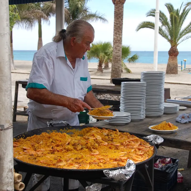 Cocinero sirviendo paella de una gran paellera junto a la playa de Burriana