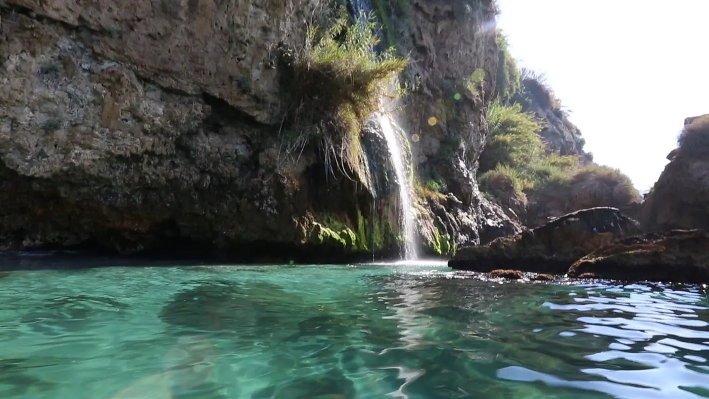 Cascada que cae al mar sobre agua turquesa en los acantilados de Maro