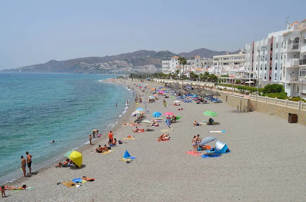 Bañistas y sombrillas en la playa El Chucho en verano, con los montes al fondo