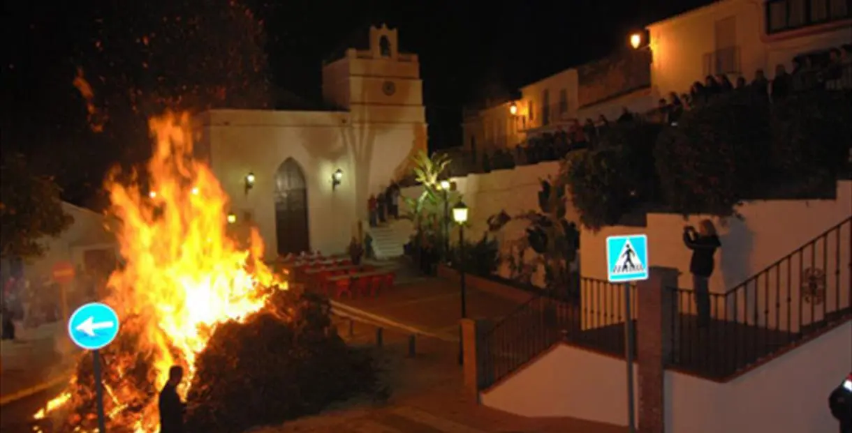 Hoguera encendida de noche junto a la iglesia de Maro, con vecinos mirando desde la barandilla