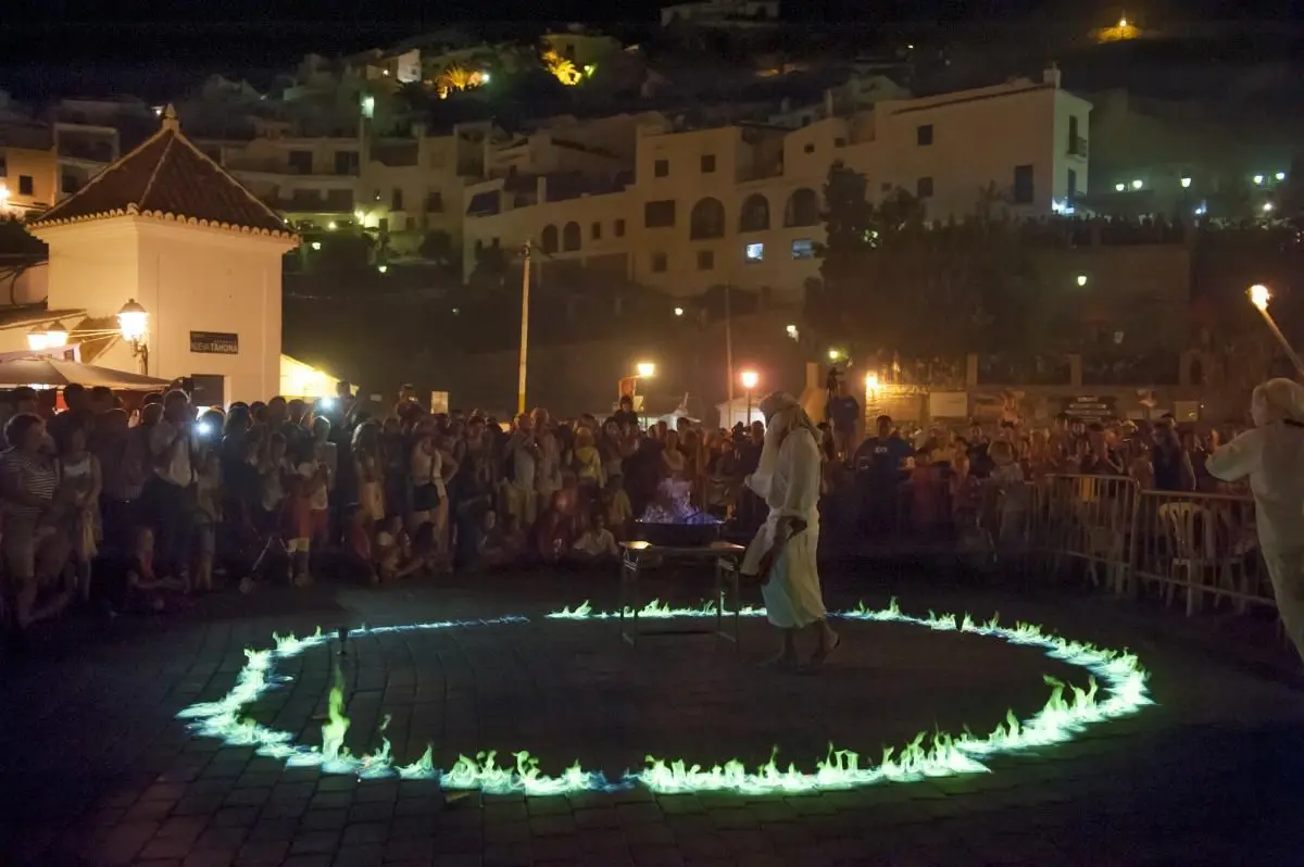Espectáculo de fuego de noche con un círculo de llamas ante el público y el pueblo iluminado