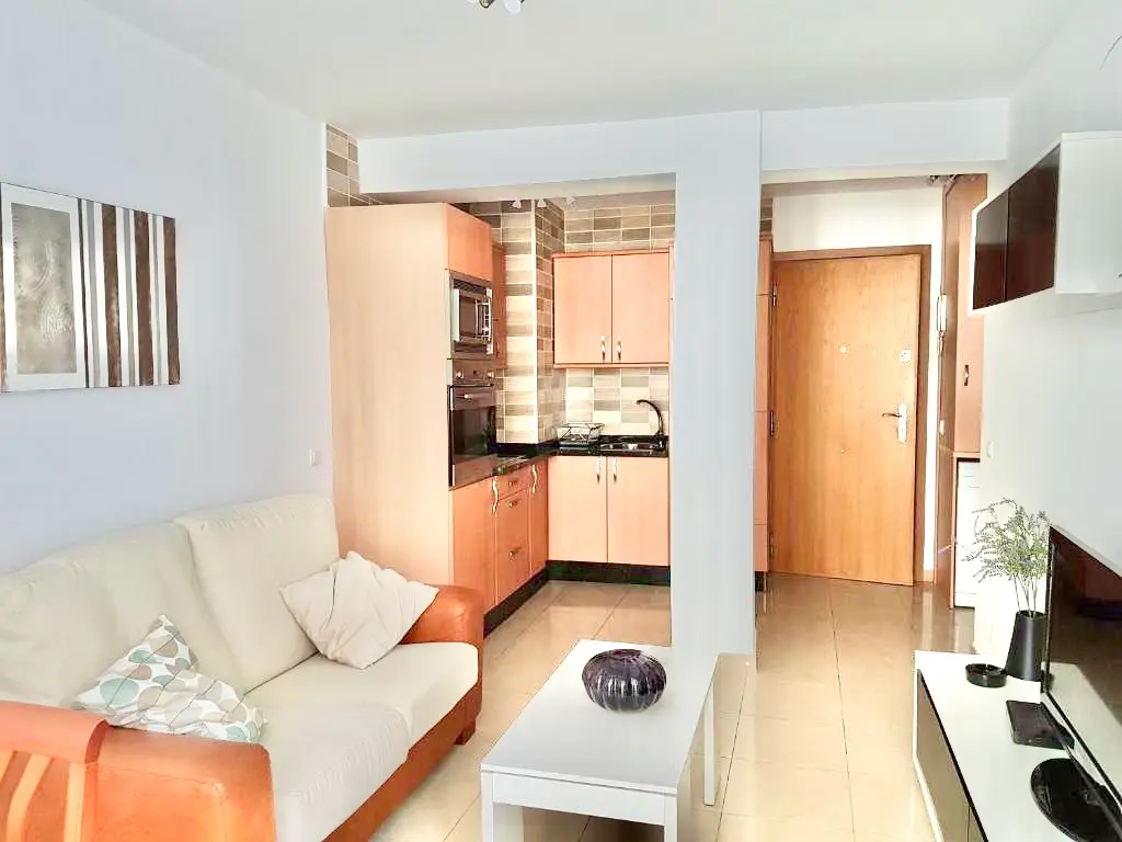 Salón con sofá, mesa de centro blanca y cocina abierta al fondo