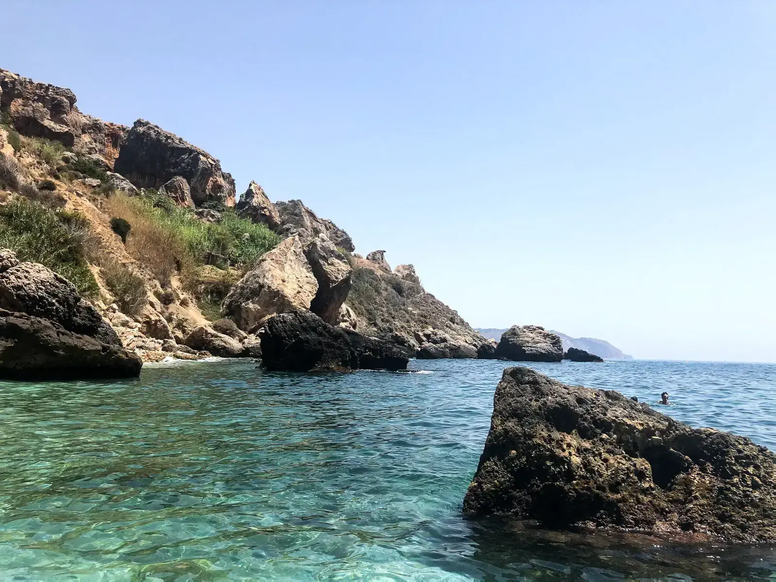 Rocas que asoman del agua turquesa en la cala Barranco de Maro, bajo los acantilados