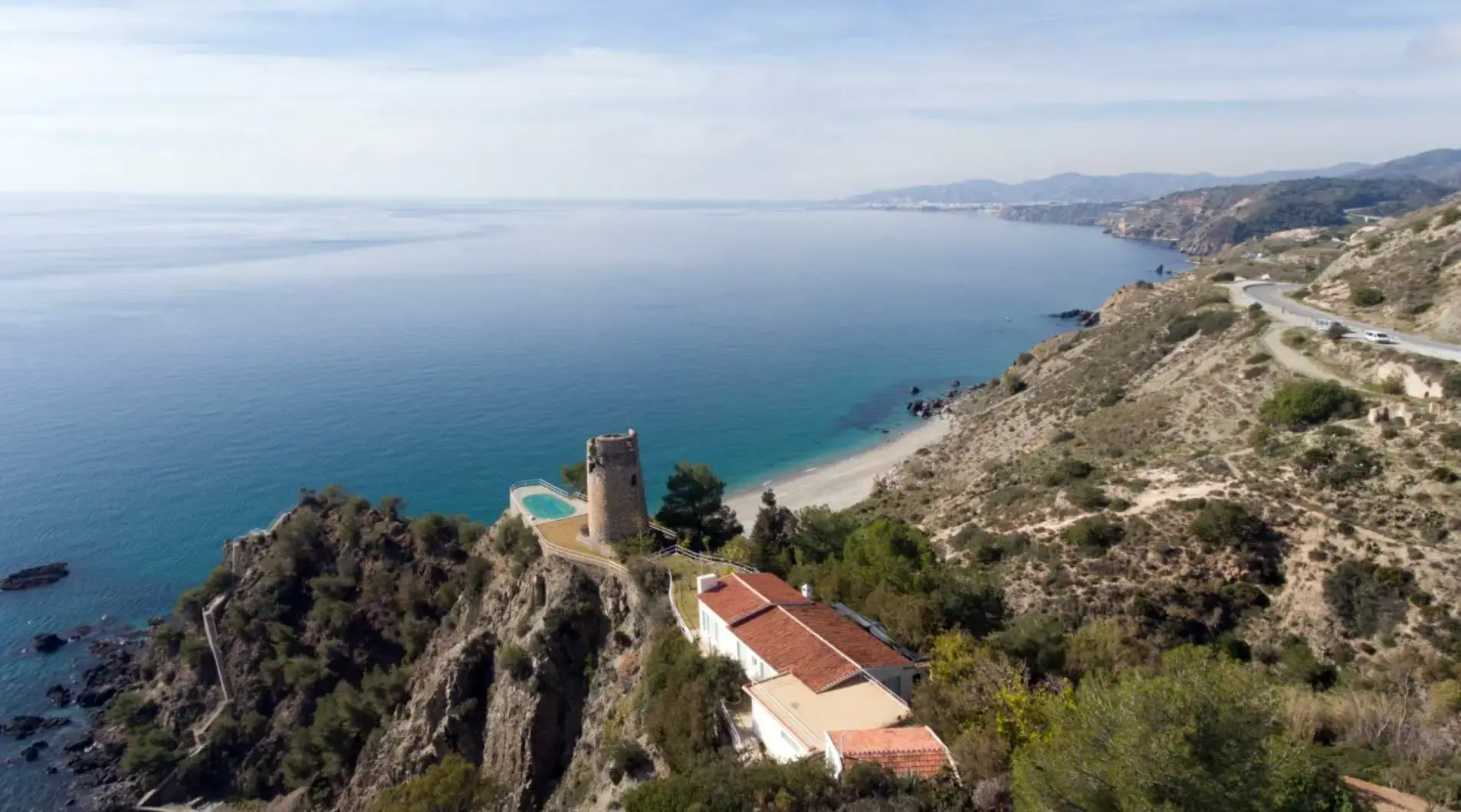 Vista aérea de la torre del Pino junto a una casa con piscina, sobre la cala y la costa de Maro