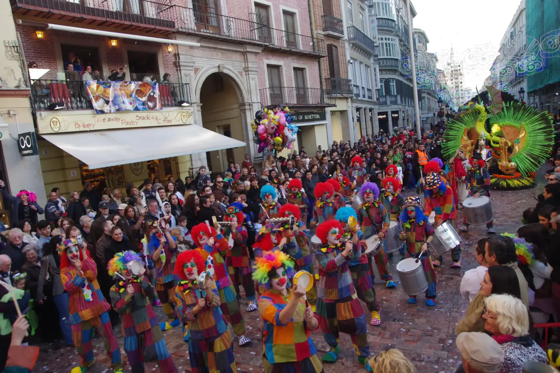 Comparsa de payasos con pelucas de colores y tambores desfilando entre el público en carnaval