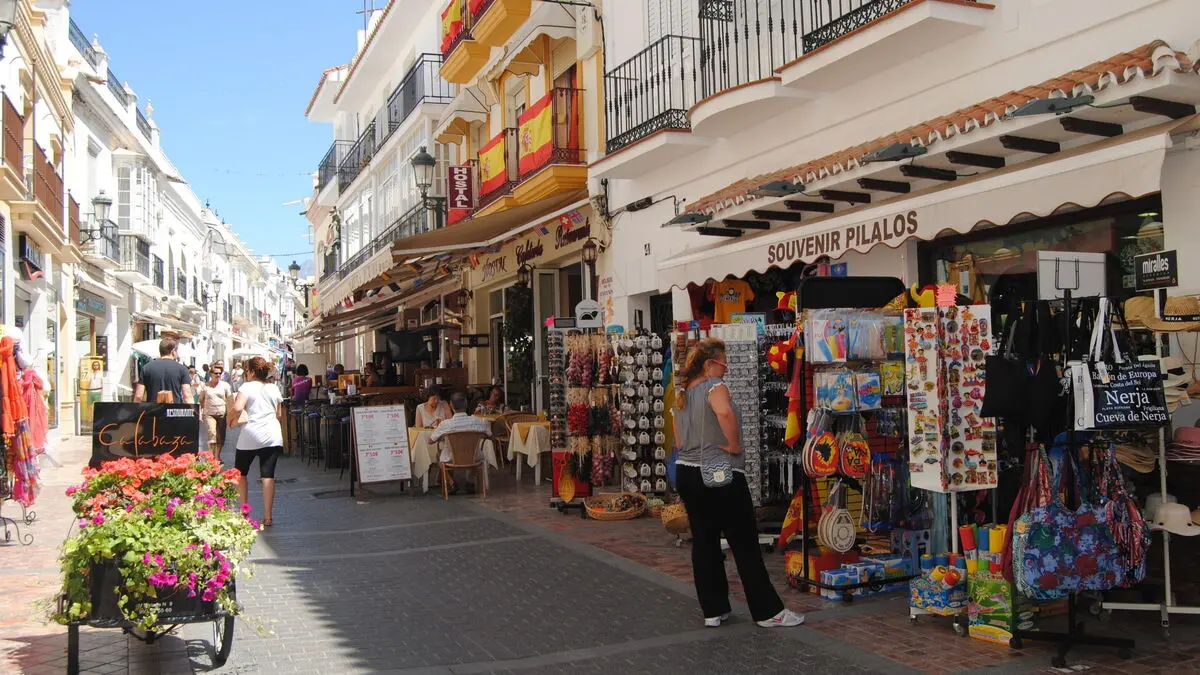 Calle comercial del centro con tiendas de recuerdos, macetas con flores y balcones con banderas