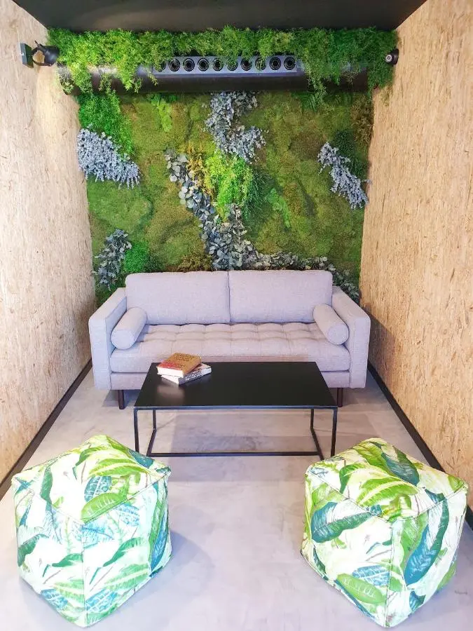 Rincón de descanso con sofá gris, mesa negra, pufs estampados y jardín vertical