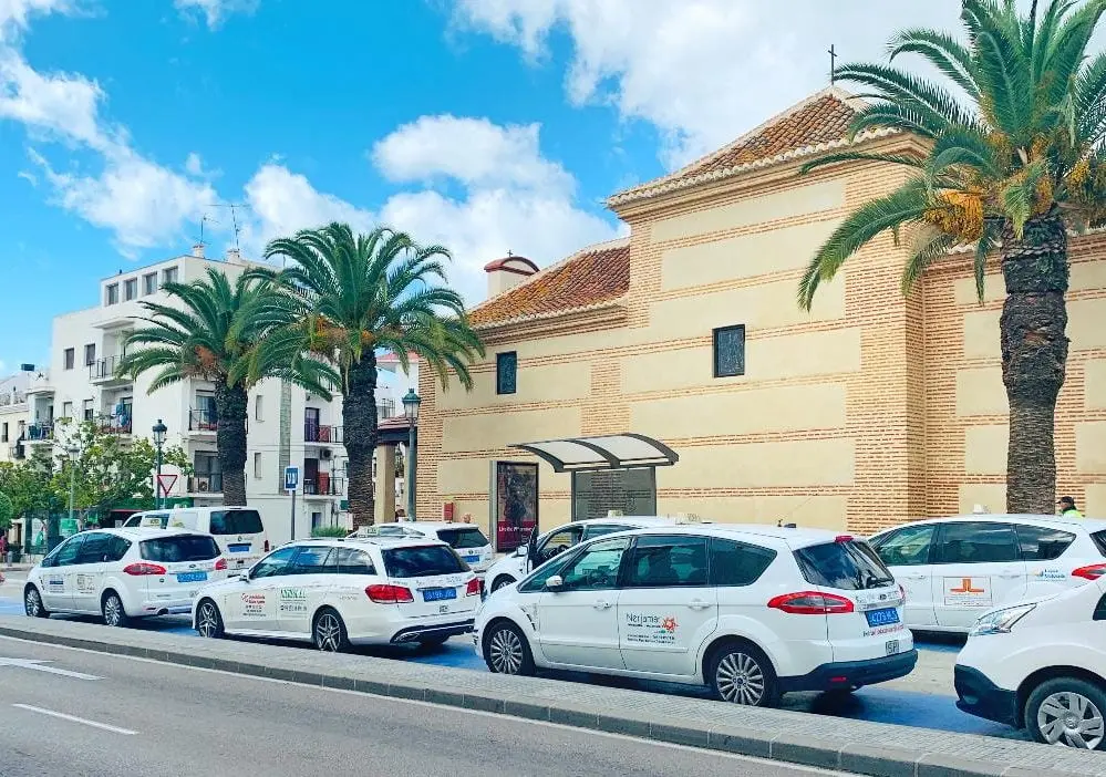 Parada de taxis blancos de Nerja junto a una ermita de ladrillo y palmeras