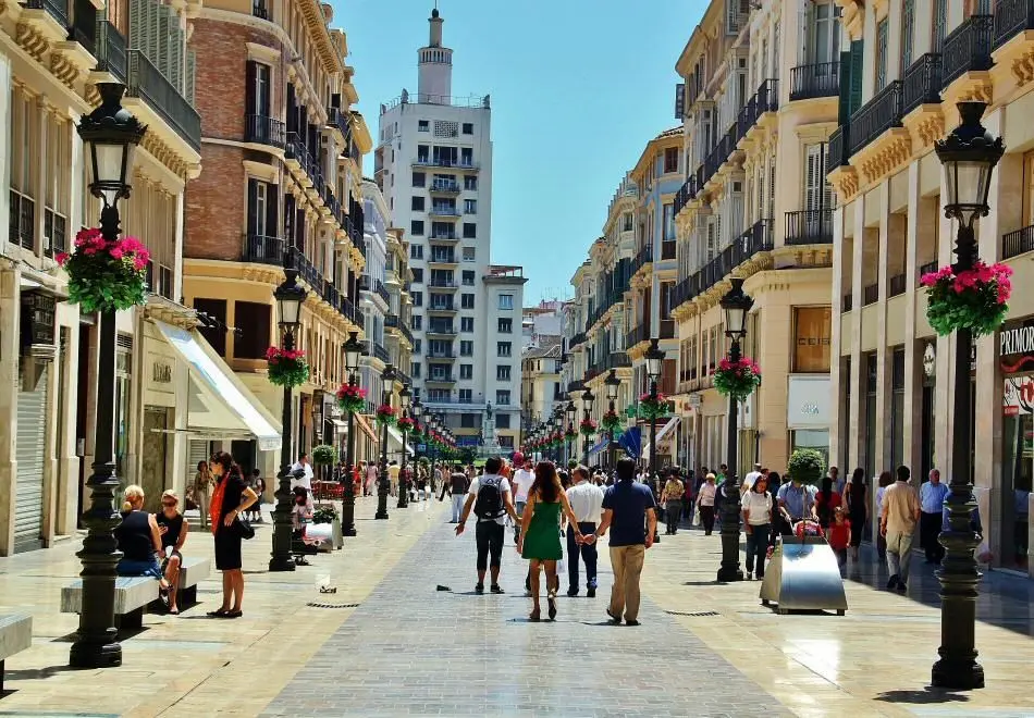 Calle Larios peatonal con farolas adornadas con flores y gente paseando en un día soleado