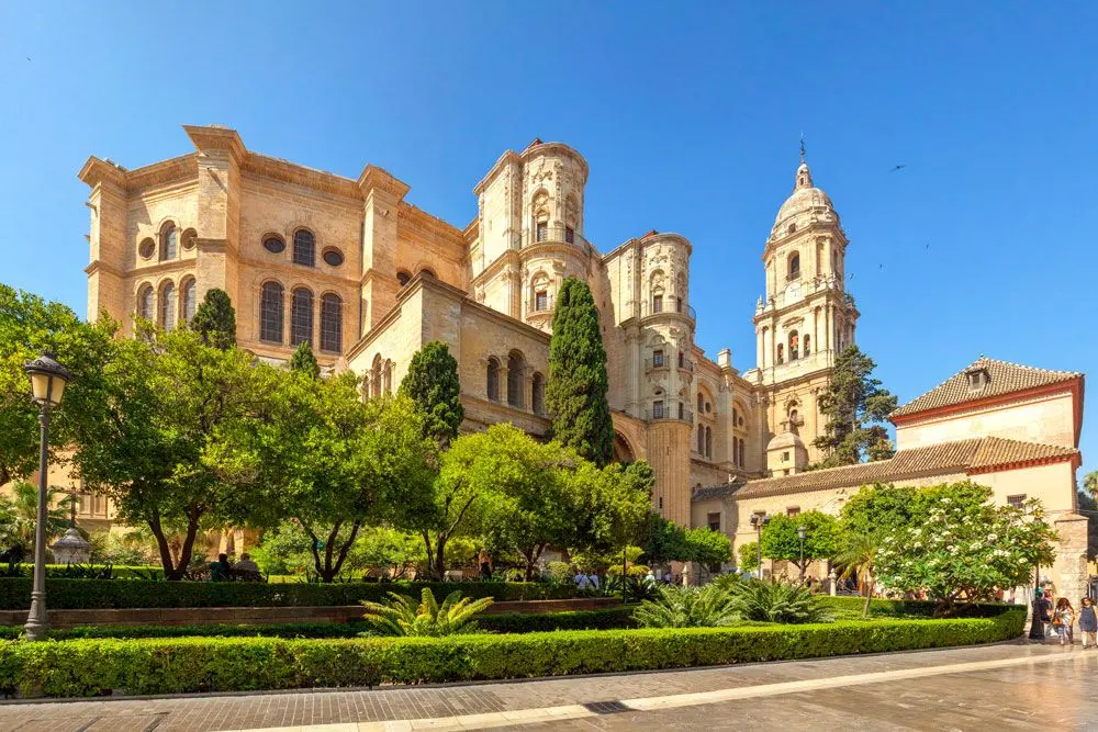 Catedral de Málaga con su torre y fachada de piedra tras los jardines