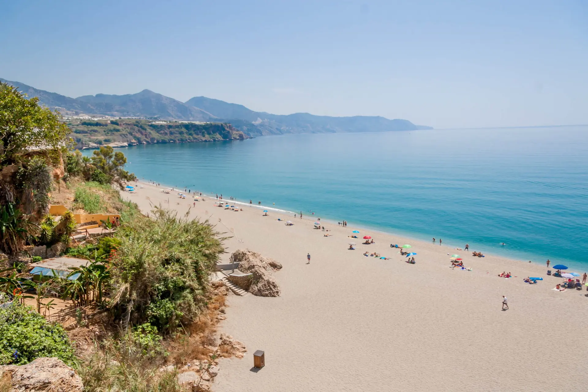 Larga playa de arena con bañistas cerca de Carabeillo, con los acantilados de Nerja al fondo