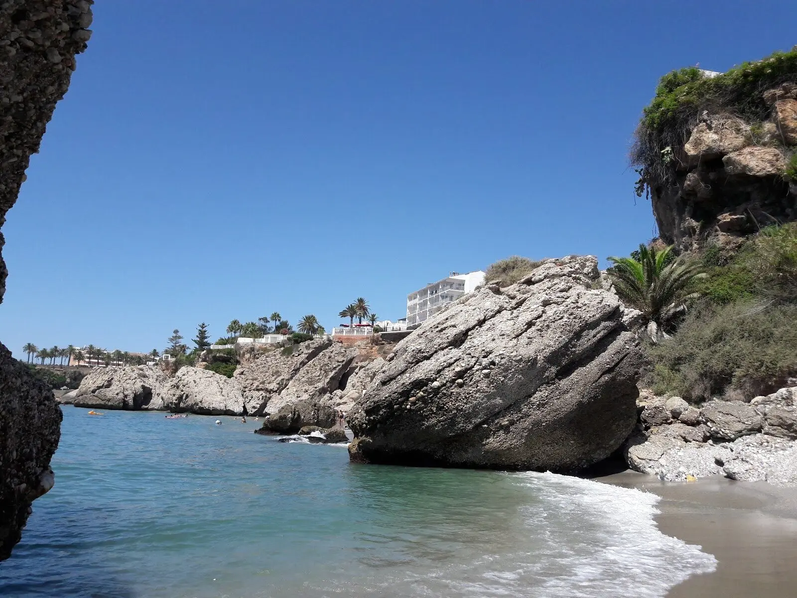 Gran roca inclinada y agua clara en la playa El Chorrillo, con edificios en lo alto