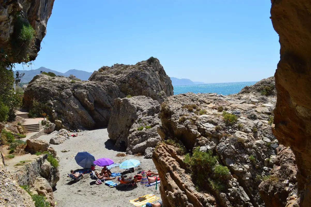 Bañistas con sombrillas en un rincón de arena entre rocas de la playa El Chorrillo
