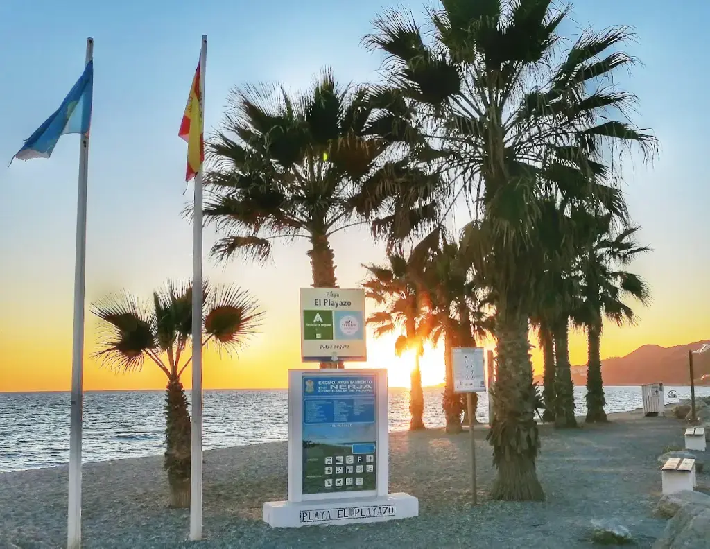 Banderas, palmeras y el cartel de la playa El Playazo al atardecer