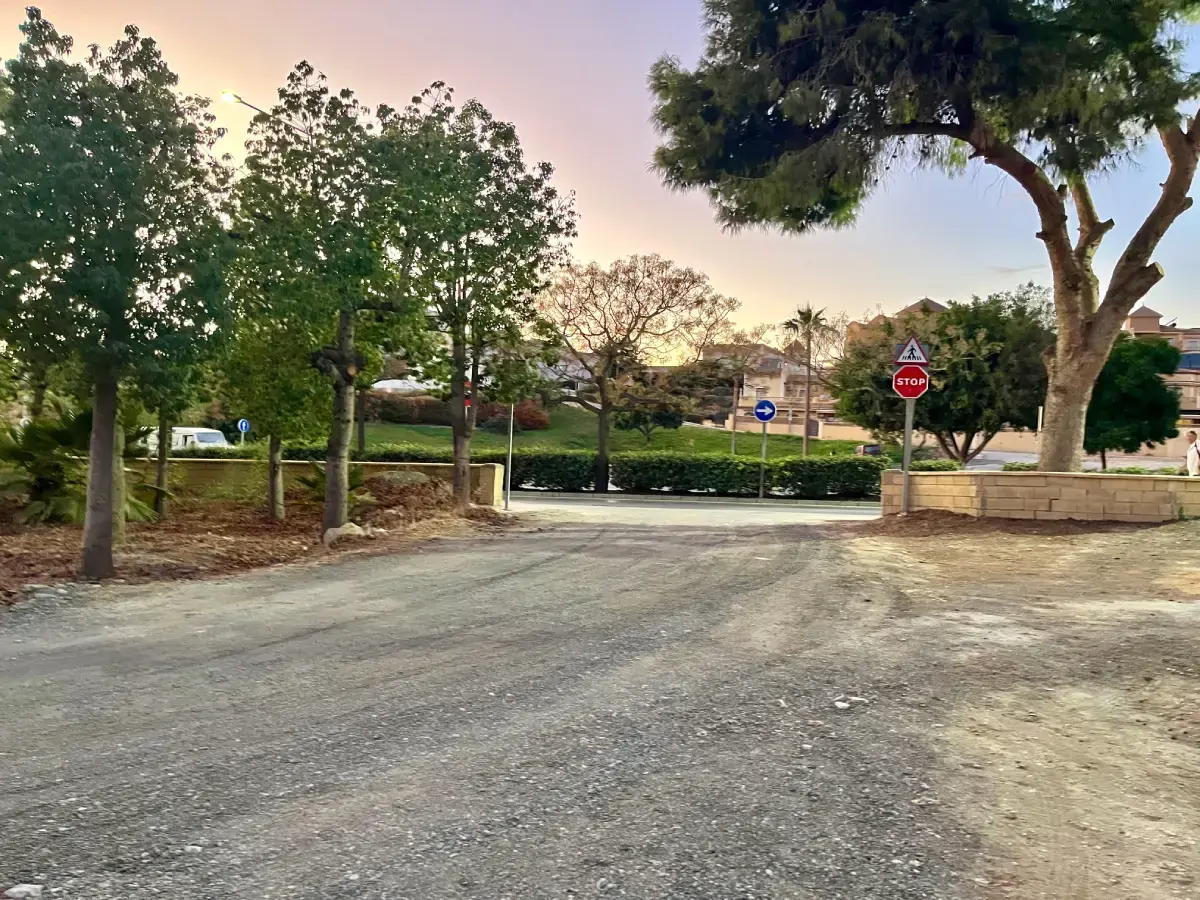 Salida del parking hacia la rotonda con señal de stop entre árboles al atardecer