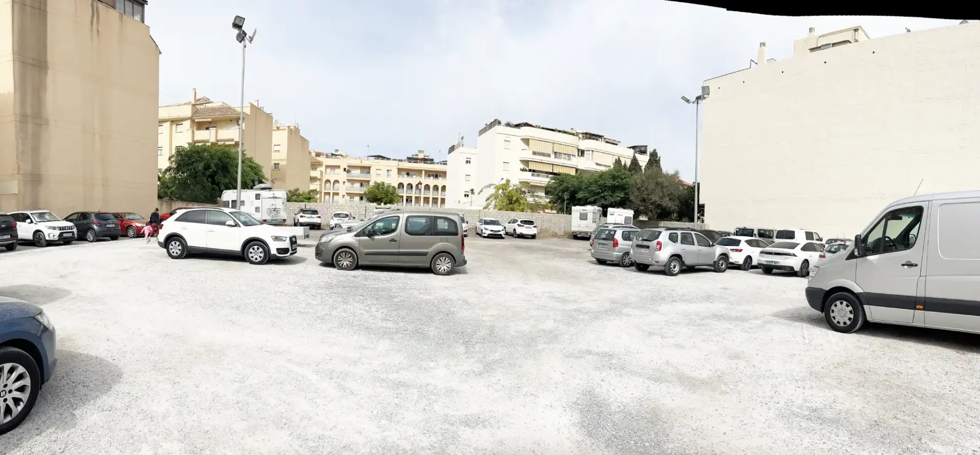 Explanada de tierra del parking con coches aparcados y edificios de apartamentos alrededor
