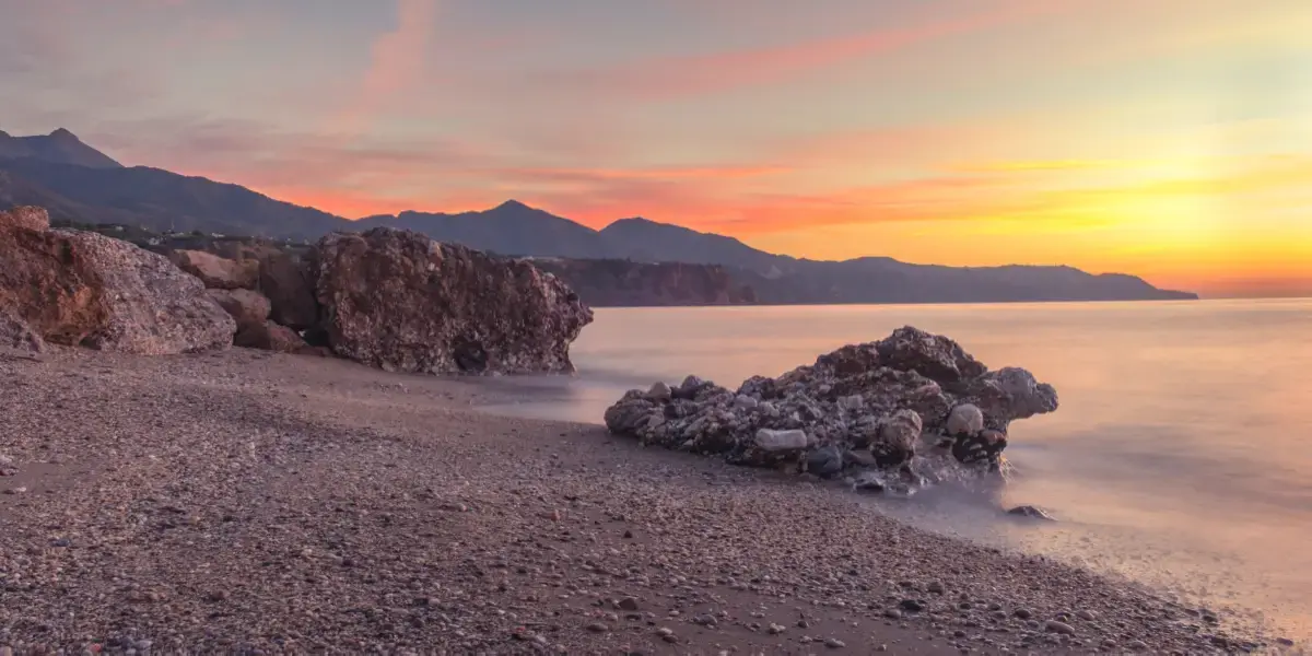 Amanecer sobre las rocas y la orilla de guijarros de la playa de Burriana