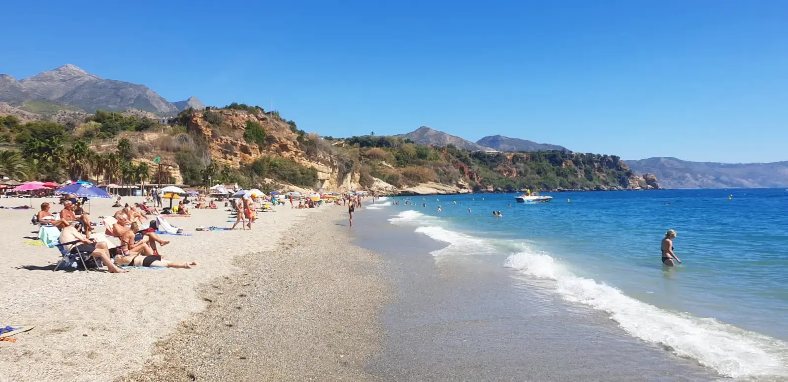 Orilla de la playa de Burriana con bañistas, una lancha y los montes de Nerja