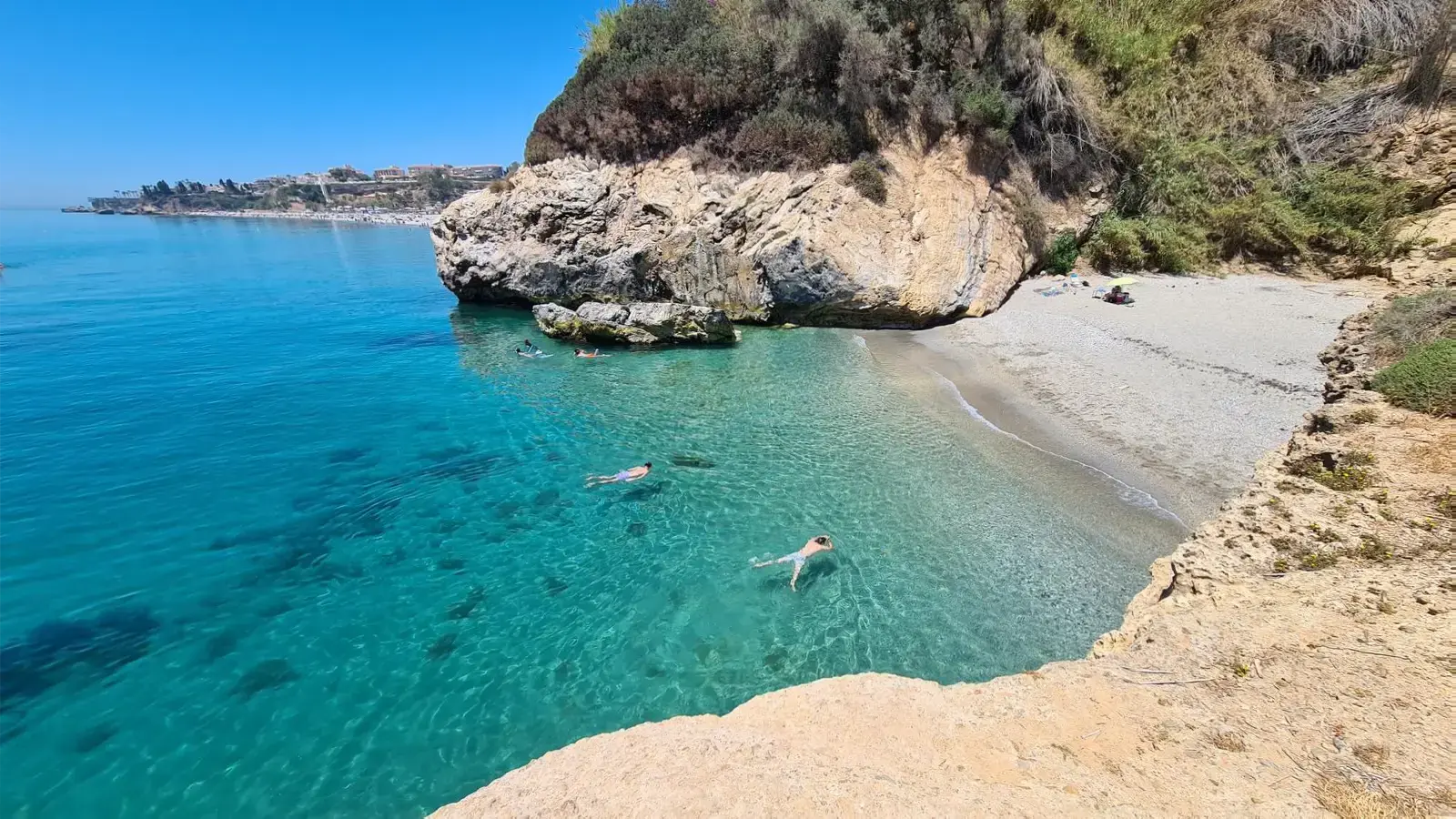Pequeña cala de aguas turquesa con bañistas nadando, cerca de la playa de Burriana