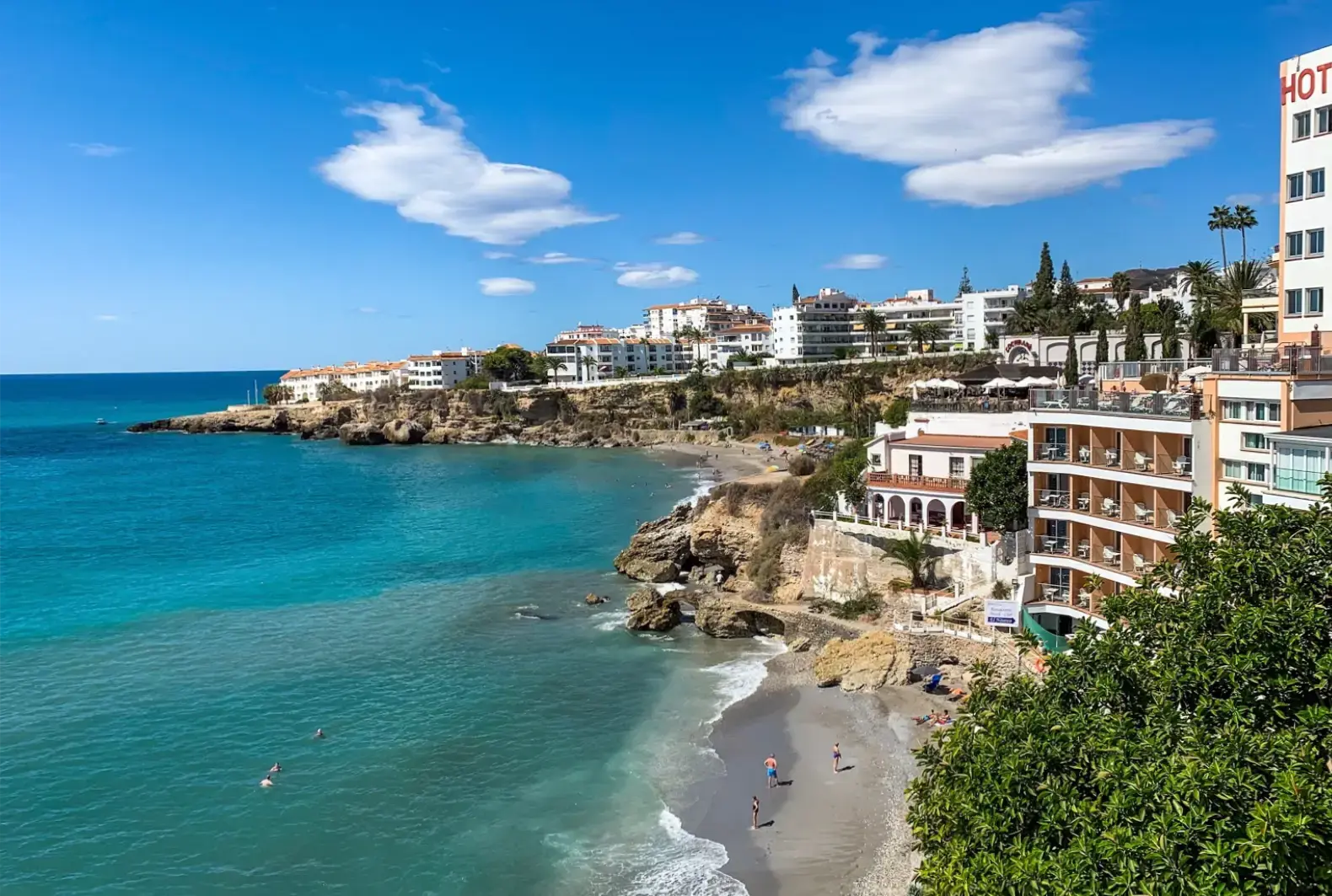 La cala La Caletilla entre rocas y hoteles, con bañistas en la orilla