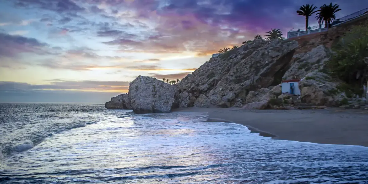 Atardecer de nubes violetas sobre la orilla y las rocas de la playa Carabeo