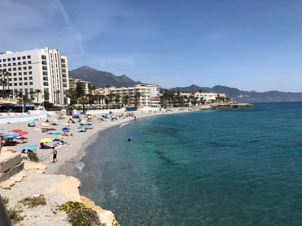 Sombrillas y bañistas en la playa La Torrecilla, con los hoteles y las sierras detrás