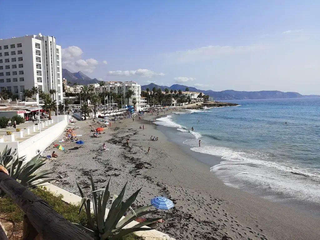 Playa La Torrecilla con oleaje suave y el paseo marítimo de Nerja