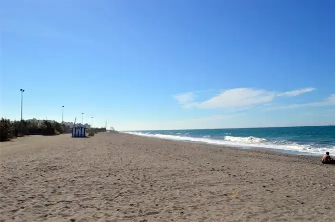 Arena amplia y casi vacía en la playa El Playazo, con olas en la orilla