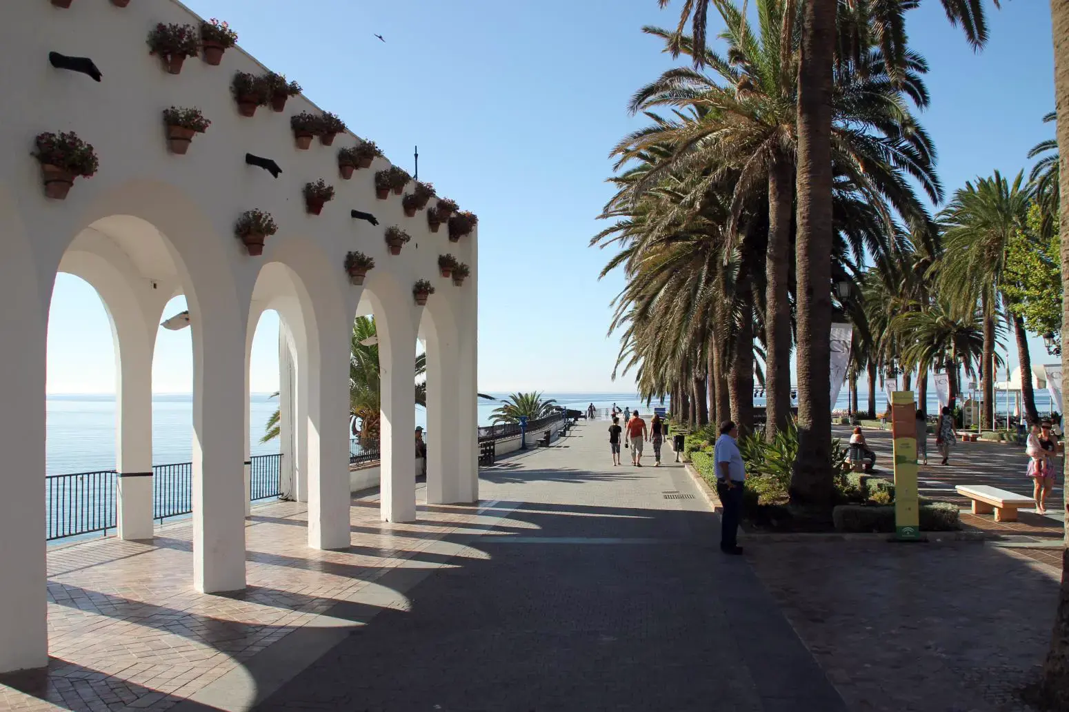 Arcos blancos con macetas en el paseo del Balcón de Europa, junto a palmeras y el mar