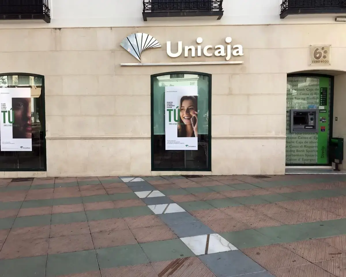 Fachada clara de la oficina de Unicaja con el logotipo y un cajero automático en la entrada lateral