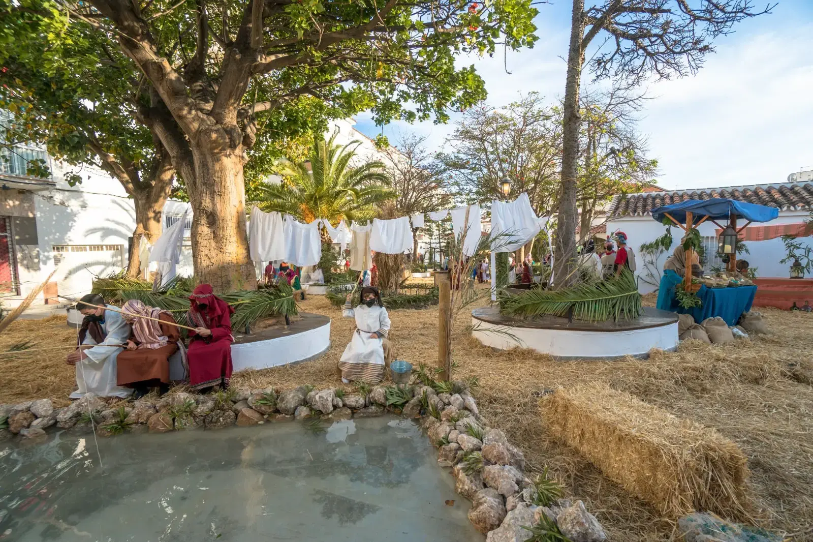 Ropa tendida, balas de paja y figurantes junto al estanque en el Belén Viviente de Las Protegidas