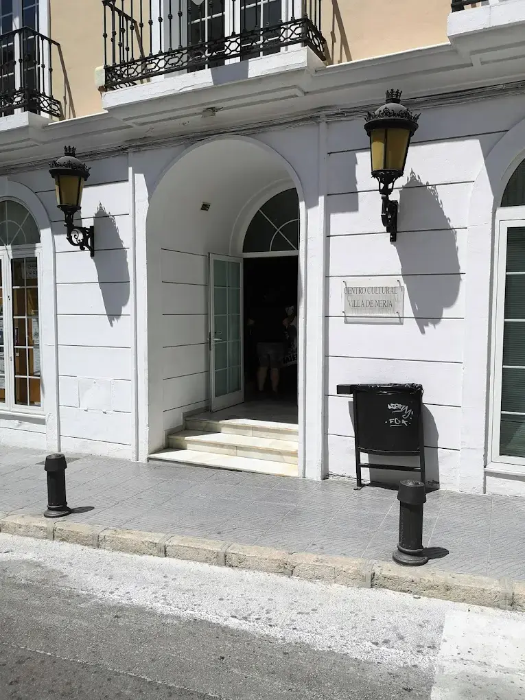 Entrada en arco con escalones y placa del centro cultural, entre farolas de pared