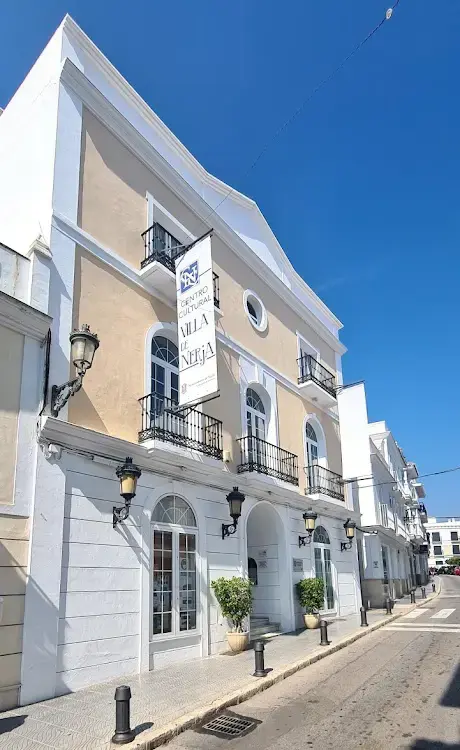 Fachada blanca y crema con balcones de forja y banderola del centro cultural