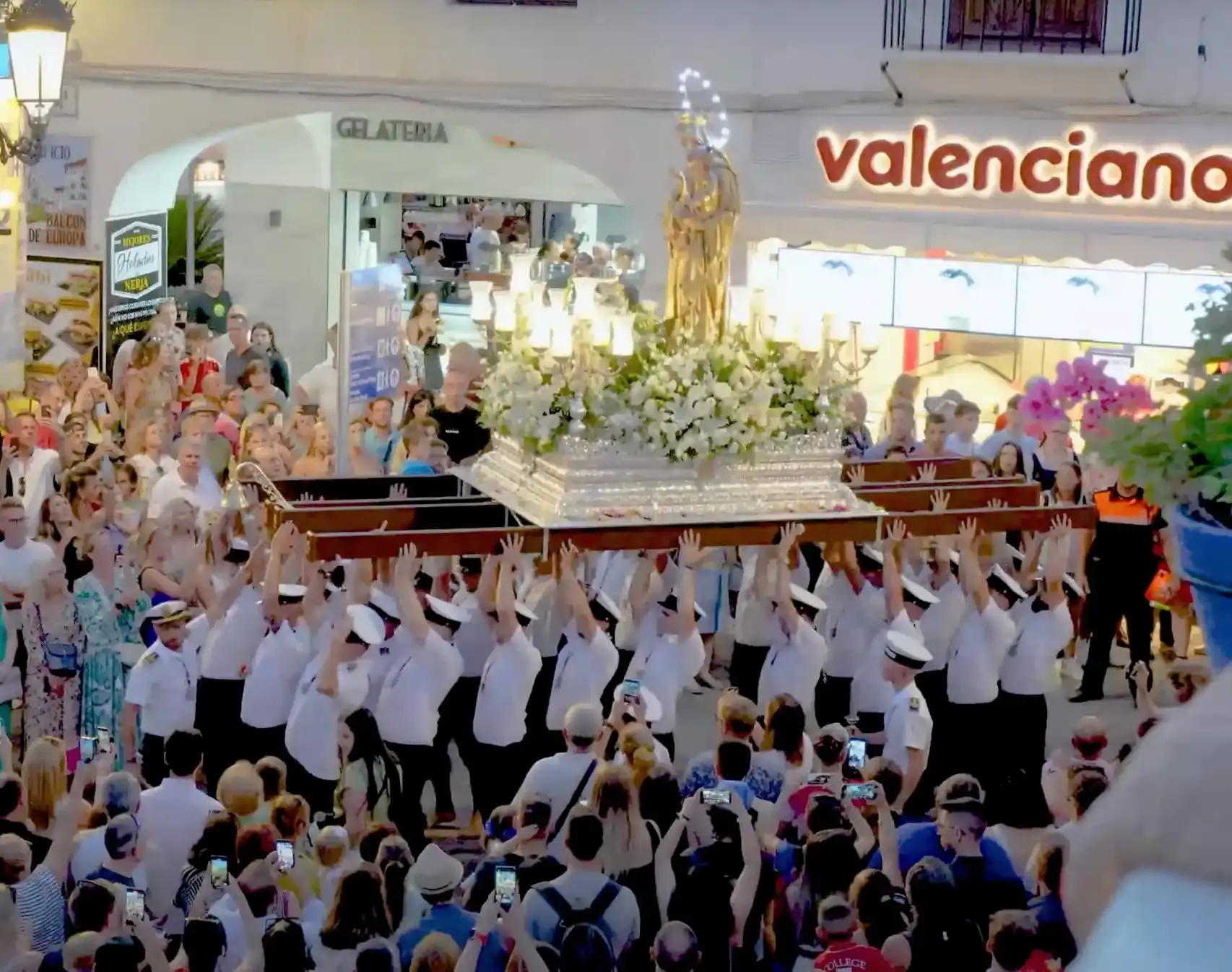 Portadores de blanco alzan el trono de la Virgen del Carmen entre una multitud por la calle