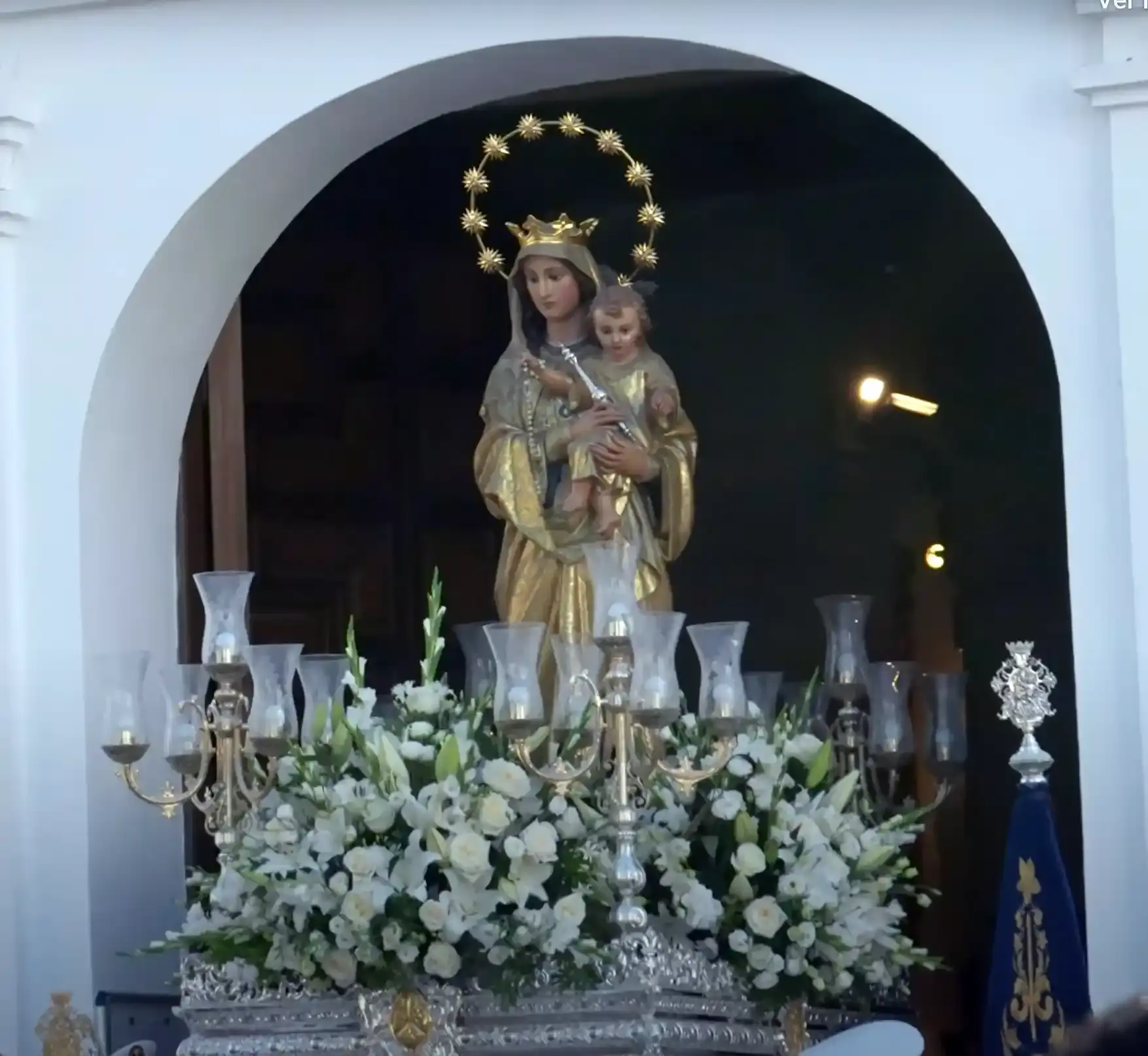 Imagen de la Virgen del Carmen con el Niño sobre su trono de flores blancas y candelabros