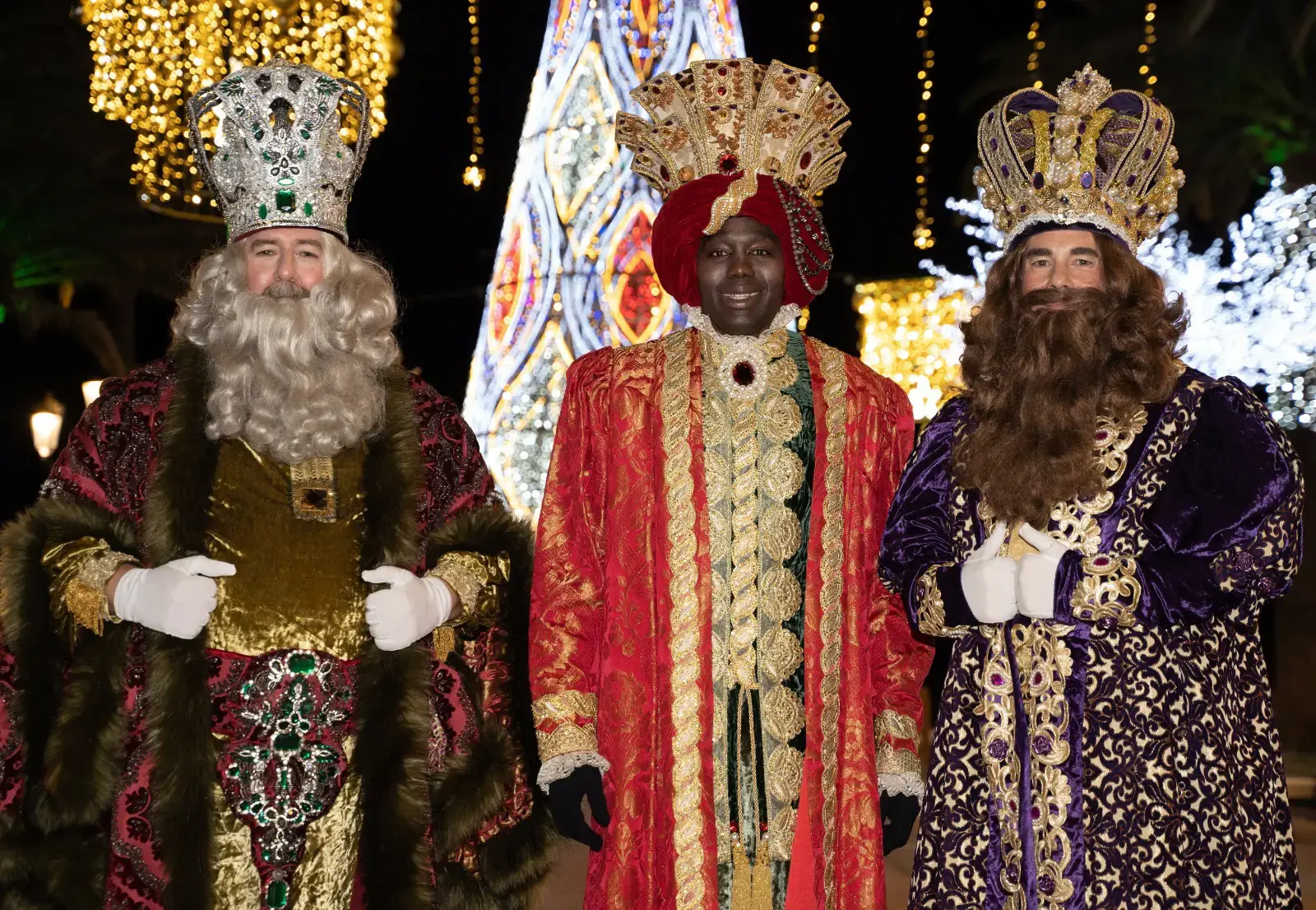 Melchor, Gaspar y Baltasar con coronas y mantos bordados ante las luces navideñas de Nerja