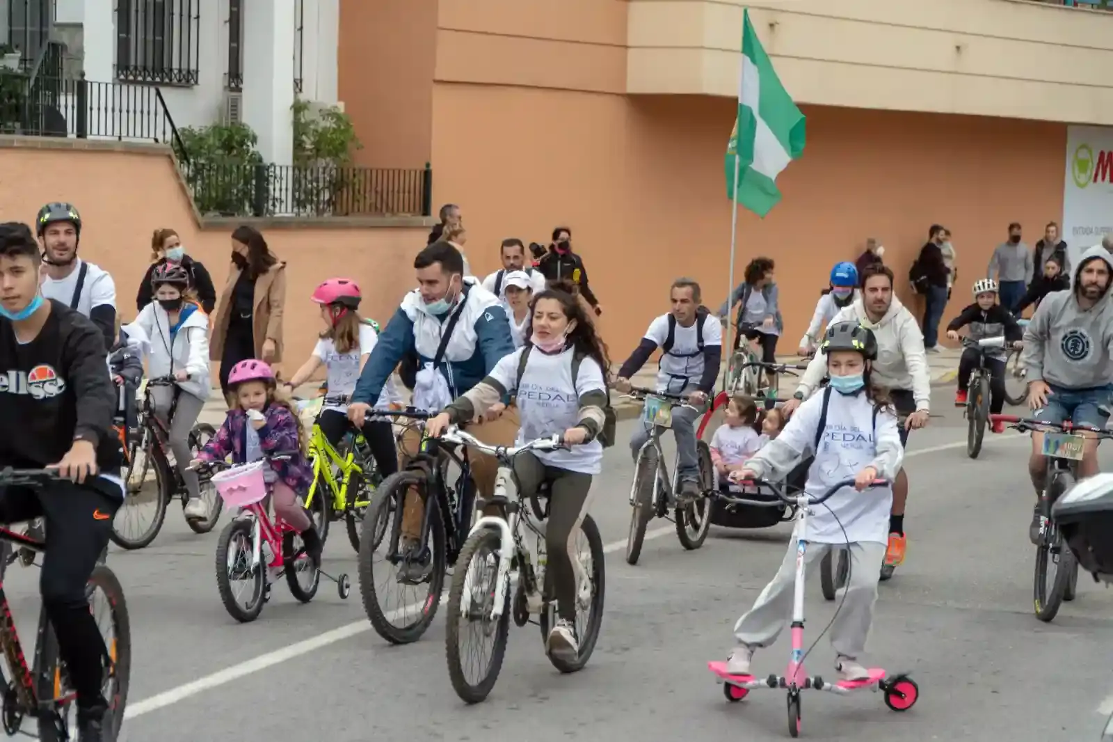 Familias en bicicleta y patinete con la bandera andaluza en la marcha del Día de Andalucía