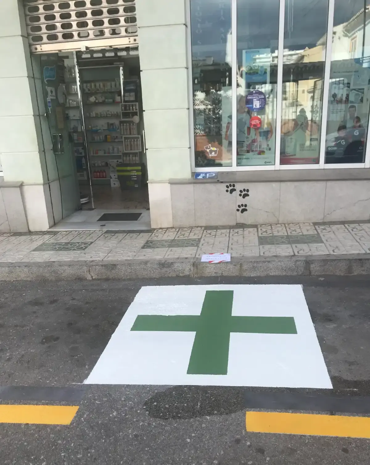 Cruz verde pintada en la plaza de aparcamiento frente a la puerta de la farmacia