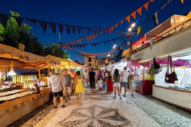 Calle empedrada con puestos de artesanía y banderines de colores durante una fiesta nocturna