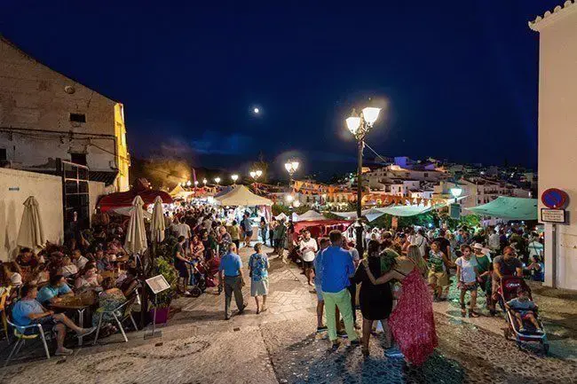 Calle llena de gente, terrazas y carpas en una noche de fiesta con luna