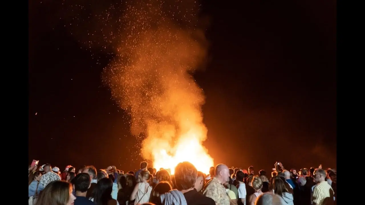 Multitud mirando una gran hoguera que lanza chispas al cielo nocturno