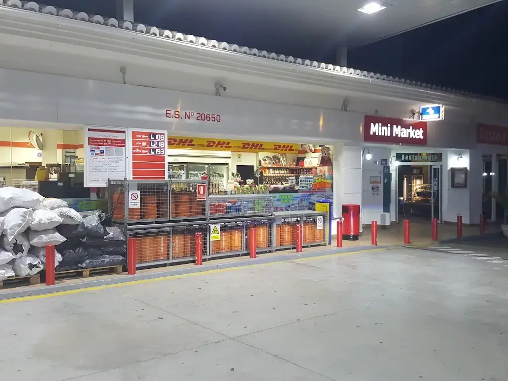 Tienda Mini Market de la gasolinera de noche, con bombonas de gas y sacos de carbón en la entrada